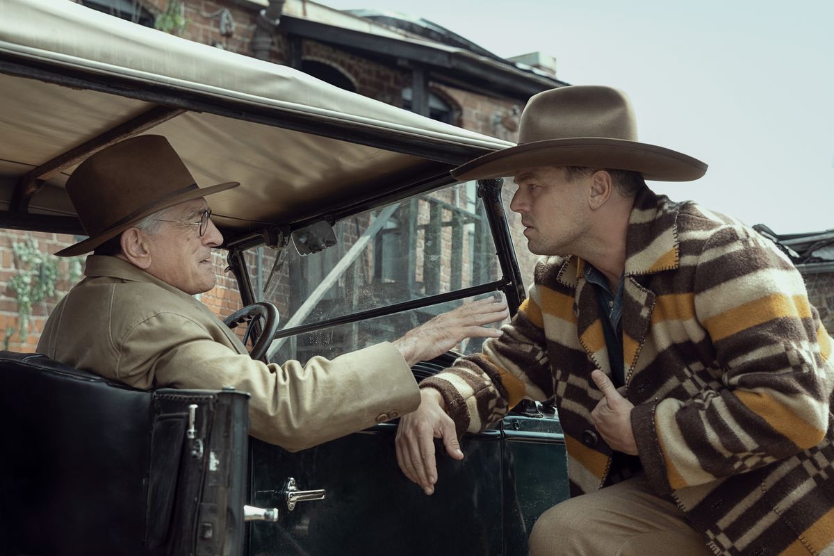 Leonardo DiCaprio avec un chapeau de cowboy et un poncho se penche sur une automobile conduite par Robert DeNiro dans Killers of the Flower Moon.