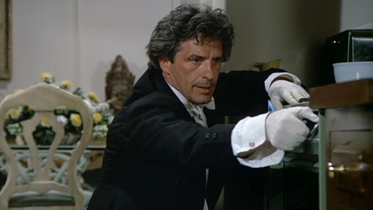John Cassavetes, vêtu d'un costume noir et de gants blancs, tente de dissimuler un meurtre qu'il a commis dans l'épisode Columbo Étude in Black 