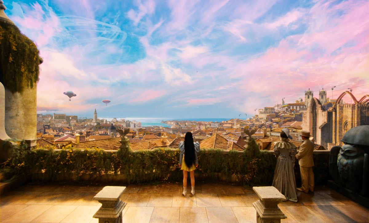 Emma Stone dans le rôle de Bella Baxter se tient devant une vue fantastique et colorée de la ville de Lisbonne dans Poor Things