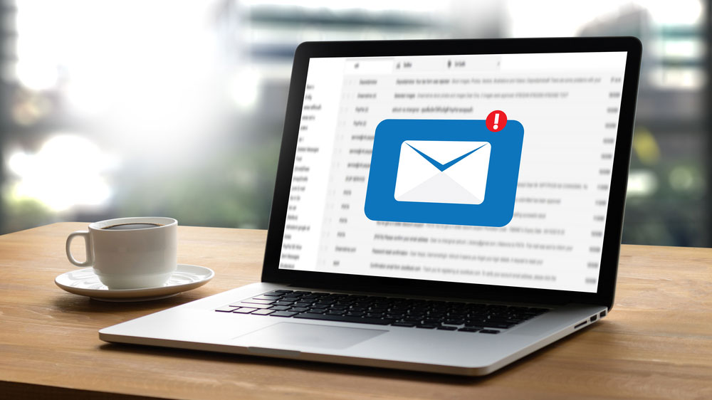 Une boîte de réception de courrier électronique affichée sur l'écran d'un ordinateur portable, à côté d'une tasse de café.