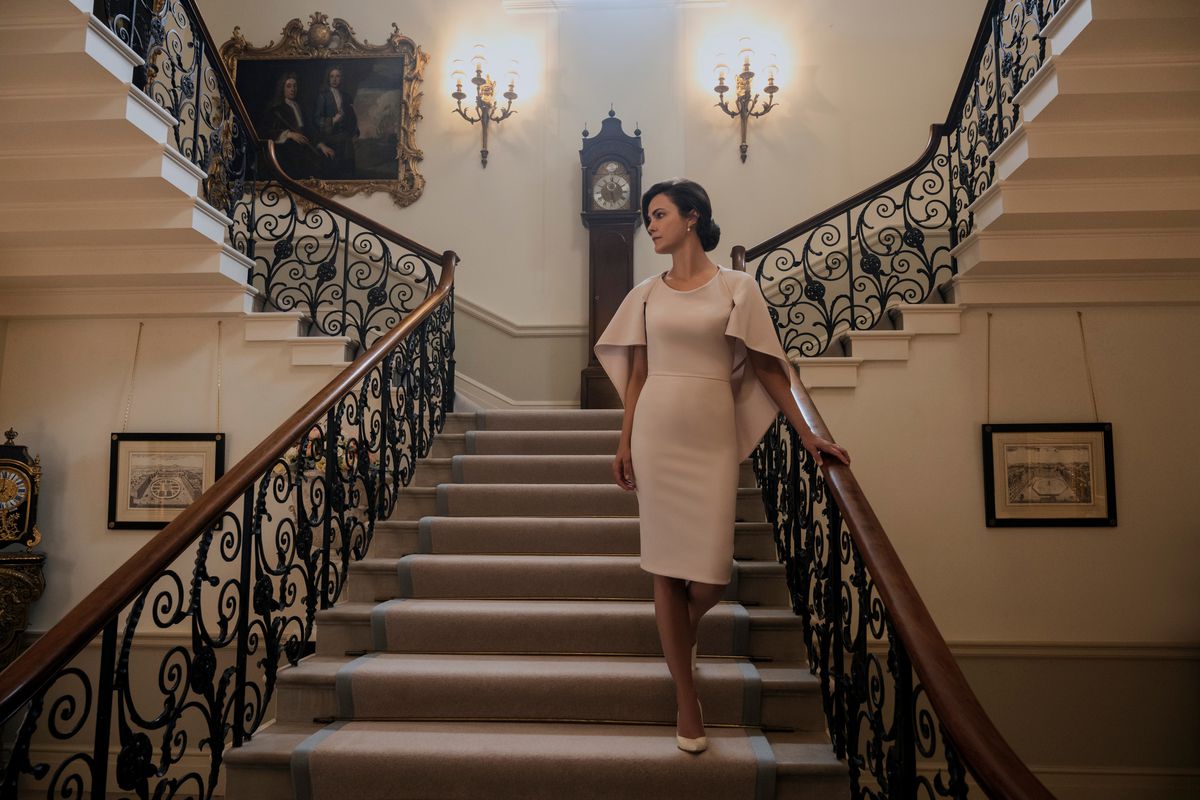 Keri Russell descend un escalier extravagant tout en portant une robe fantaisie beige dans The Diplomat.