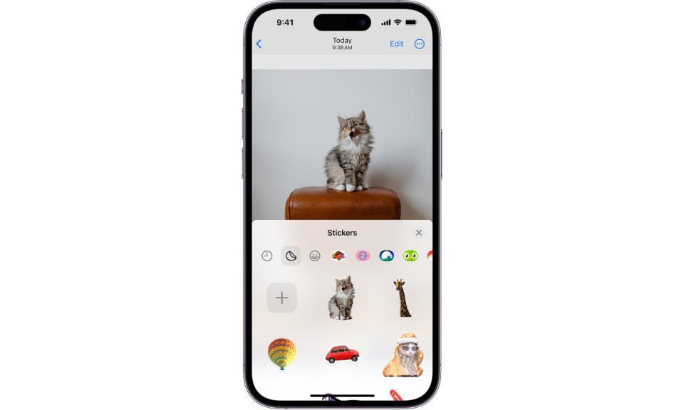 Une capture d'écran à l'intérieur d'un cadre iPhone, montrant le menu contextuel Autocollants dans l'application iOS Photos.  Un chat bâille sur la photo, et le tiroir de stickers ci-dessous le montre entre autres (dont une girafe, un ballon, une voiture, etc.).