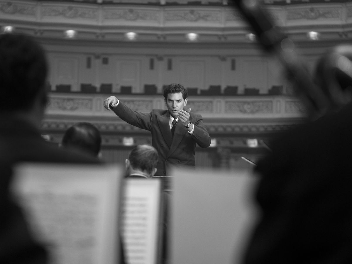 Bradley Cooper dirigeant un orchestre vu depuis la rangée du milieu dans une scène en noir et blanc de Maestro de Netflix