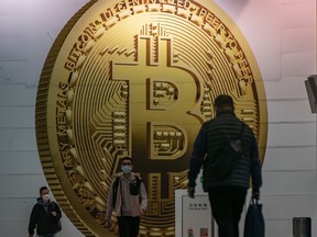 Des piétons passent devant une publicité affichant un jeton de crypto-monnaie Bitcoin à Hong Kong, en Chine.