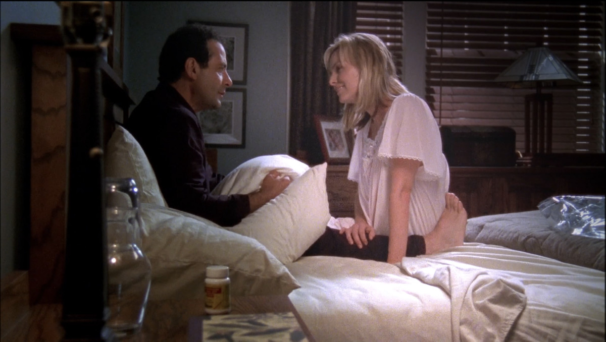 Monk (Tony Shalhoub) tenant l'oreiller de Trudy et ayant l'air triste tandis que son fantôme (Melora Hardin) est assis devant lui en souriant