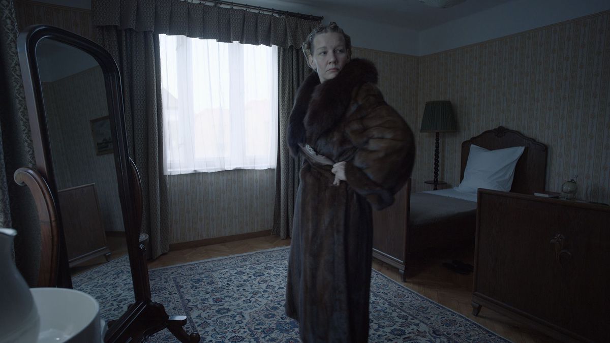 Sandra Huller dans le rôle d'Hedwig Höss dans The Zone of Interest, se regardant dans un miroir tout en portant un manteau de fourrure