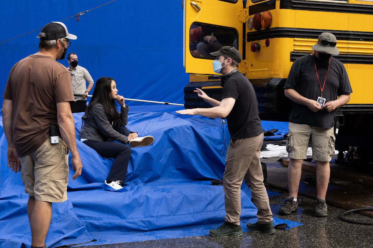 Matt Shakman discutant avec Anna Sawai sur le tournage de Monarch ;  elle est assise sur un écran bleu géant à côté d'un bus scolaire jaune