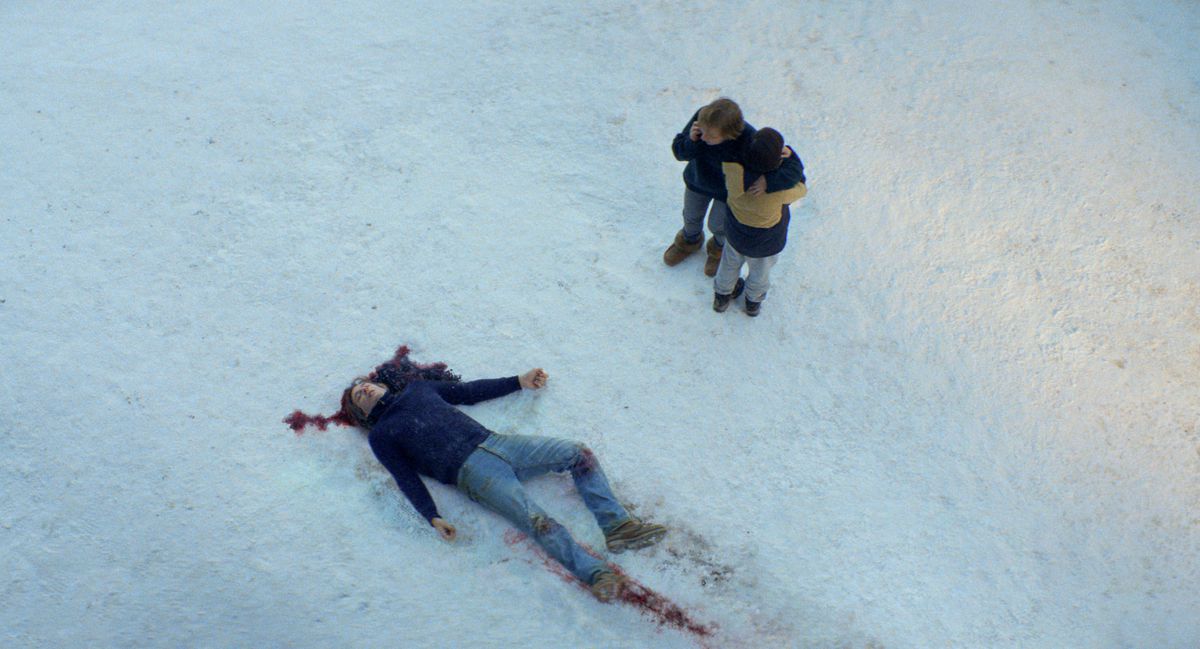 Un corps mort et ensanglanté dans la neige dans Anatomy of a Fall, alors qu'une personne proche parle au téléphone