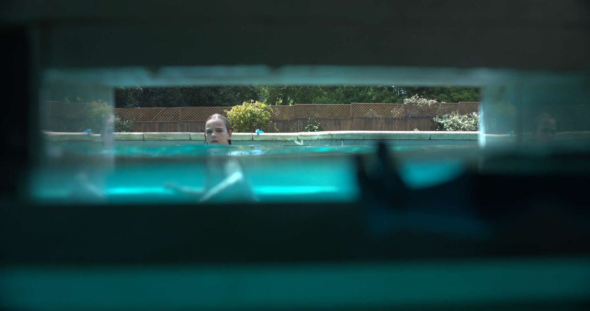Un enfant regarde vers un écumeur de piscine, que nous voyons du point de vue de l'écumeur dans Night Swim