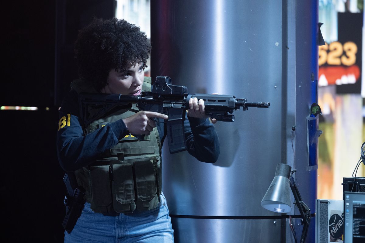 Emmy Raver-Lampman, vêtue d'un gilet pare-balles et d'un uniforme du FBI, vise un fusil d'assaut dans The Beekeeper.