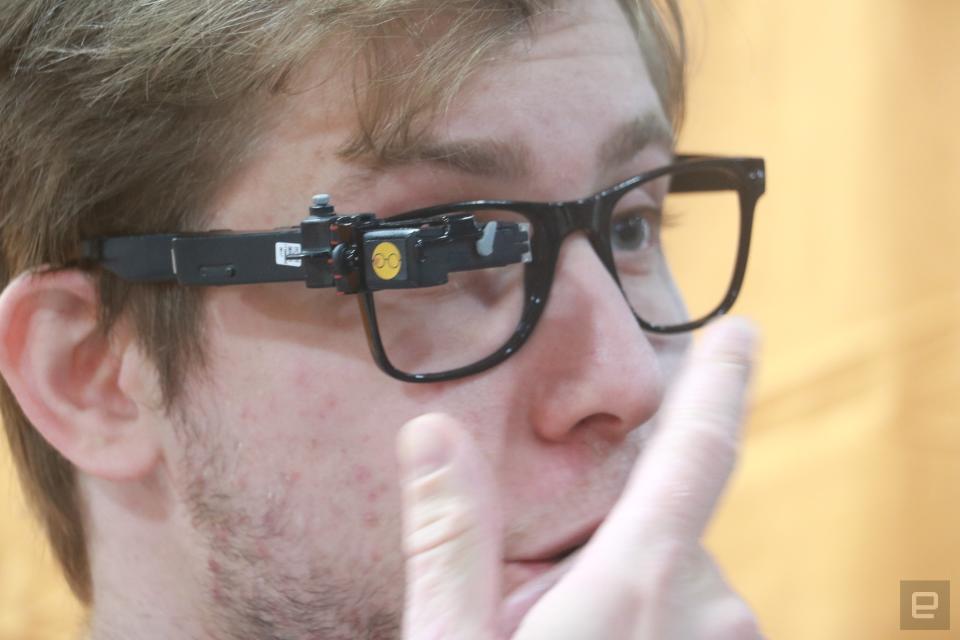 Une personne portant le TranscribeGlass sur le côté droit d’une paire de lunettes à monture noire. 