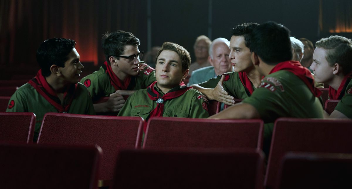 Sammy Fabelman (Gabriel LaBelle), un adolescent vêtu d'un uniforme scout vert et d'un foulard rouge, est assis dans une salle de cinéma en train de regarder son dernier projet de film, avec tous ses copains scouts assis autour de lui et lui parlant dans Les Fabelman de Steven Spielberg.