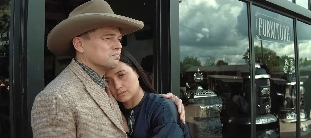 Ernest (Leonardo DiCaprio, en costume beige et chapeau de cowboy) réconforte sa femme Mollie (Lily Gladstone) alors qu'elle s'appuie contre lui devant la vitrine d'un magasin de meubles dans Killers of the Flower Moon