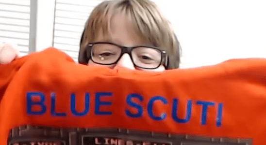 Blue Scuti holds up an orange hoodie with the words