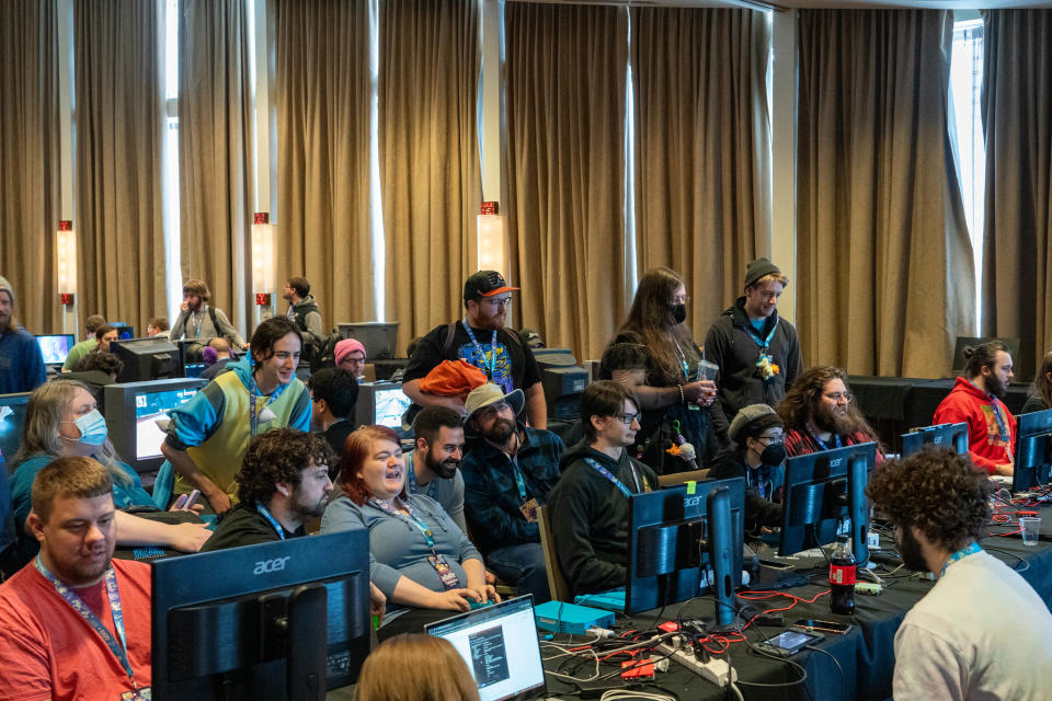 Une salle de conférence remplie de joueurs et de speedrunners jouant et regardant des jeux sur différents écrans d'ordinateur.