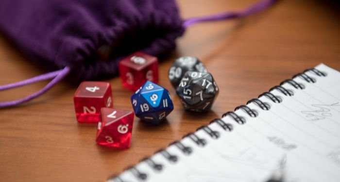 un stylo, un cahier et des dés dans une pochette en velours violet pour jouer à un jeu de rôle comme Donjons et Dragons