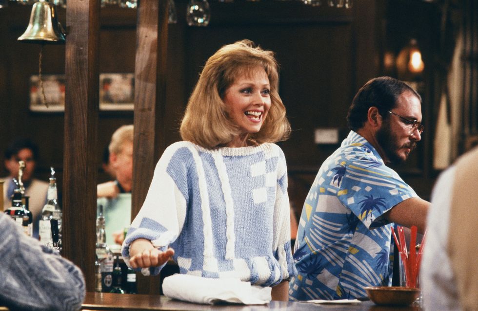 bravo Diane Chambers, jouée par Shelley Long, debout derrière le bar et souriante