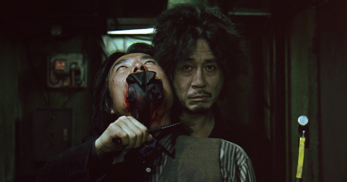 Choi Min-sik dans le rôle de Dae-su Oh tenant en otage un homme bâillonné avec un couteau et un marteau dans Oldboy.