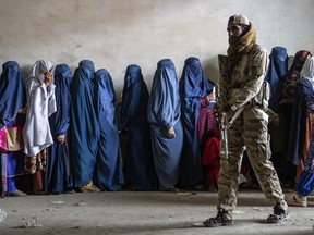Un combattant taliban monte la garde pendant que des femmes attendent de recevoir des rations alimentaires distribuées par un groupe d'aide humanitaire, à Kaboul, en Afghanistan, le 23 mai 2023.