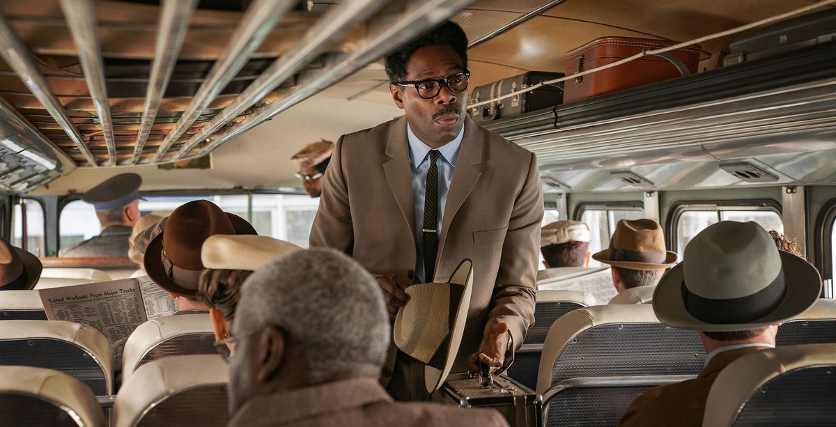 Colman Domingo, dans un costume beige avec un chapeau à la main dans le rôle de Bayard Rustin, monte à bord d'un bus complet dans le film Rustin de Netflix