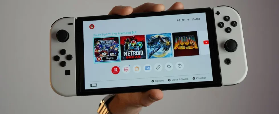A hand holds up a white Nintendo Switch showing games like Doom 64 and Metroid Dread on the screen.