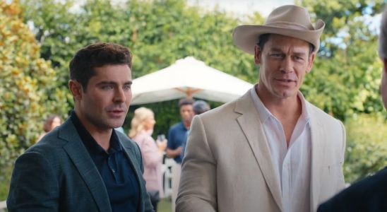 Zac Efron and John Cena standing together in conversation at a party in Ricky Stanicky.