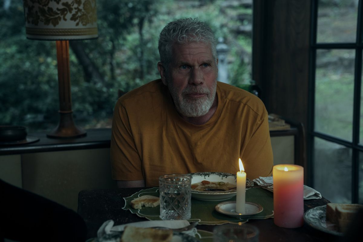 Ron Perlman a l'air triste dans un T-shirt jaune à une table aux chandelles au crépuscule dans Mr. &  Madame Smith