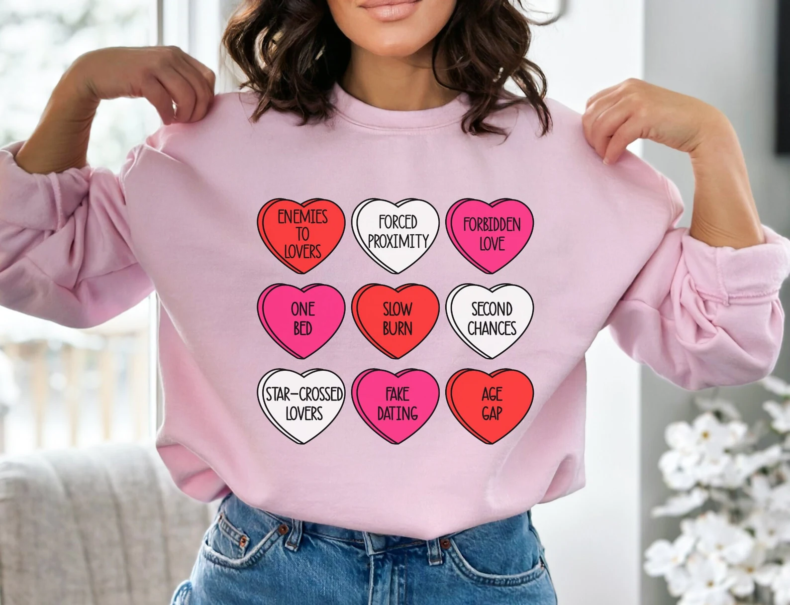 Image d'un sweat-shirt rose avec des cœurs dessus.  À l’intérieur des cœurs se trouvent des noms de tropes romantiques. 