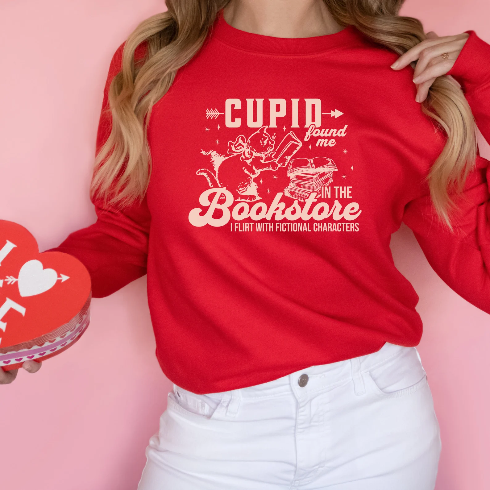 Image d'une personne blanche portant un sweat-shirt rouge qui dit "Cupidon m'a trouvé dans la librairie.  Je flirte avec des personnages fictifs."