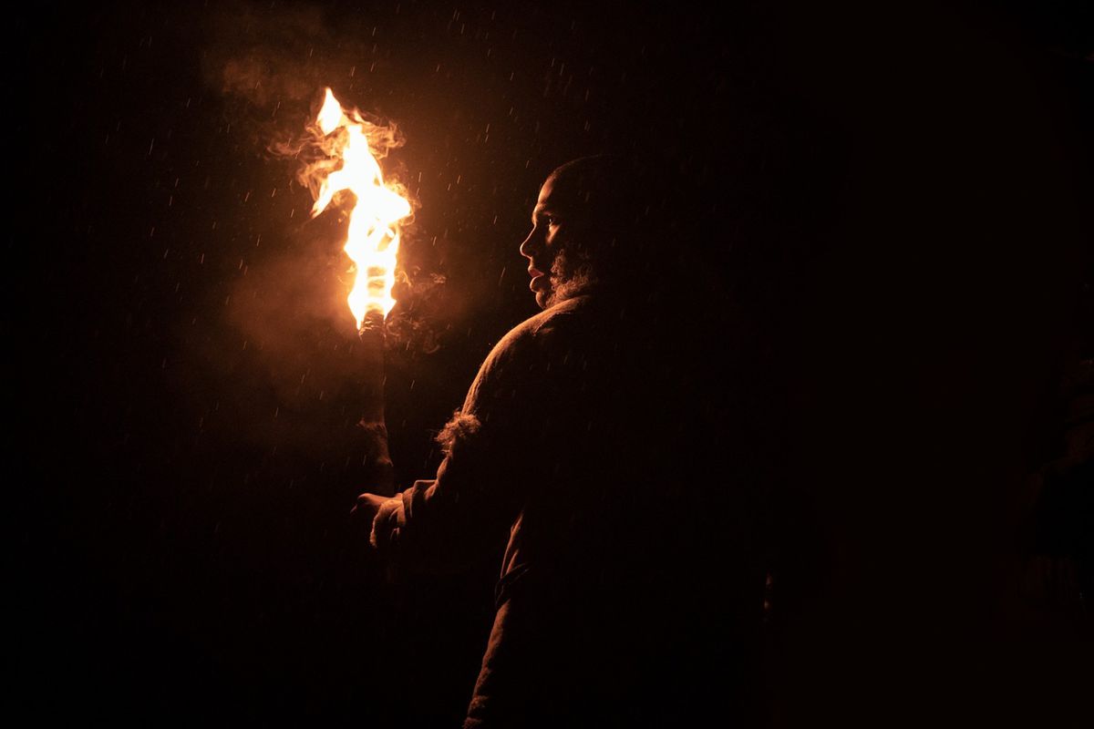 Un homme paléolithique avec une torche se tient dans l'obscurité totale, dos à la caméra dans Out of Darkness.