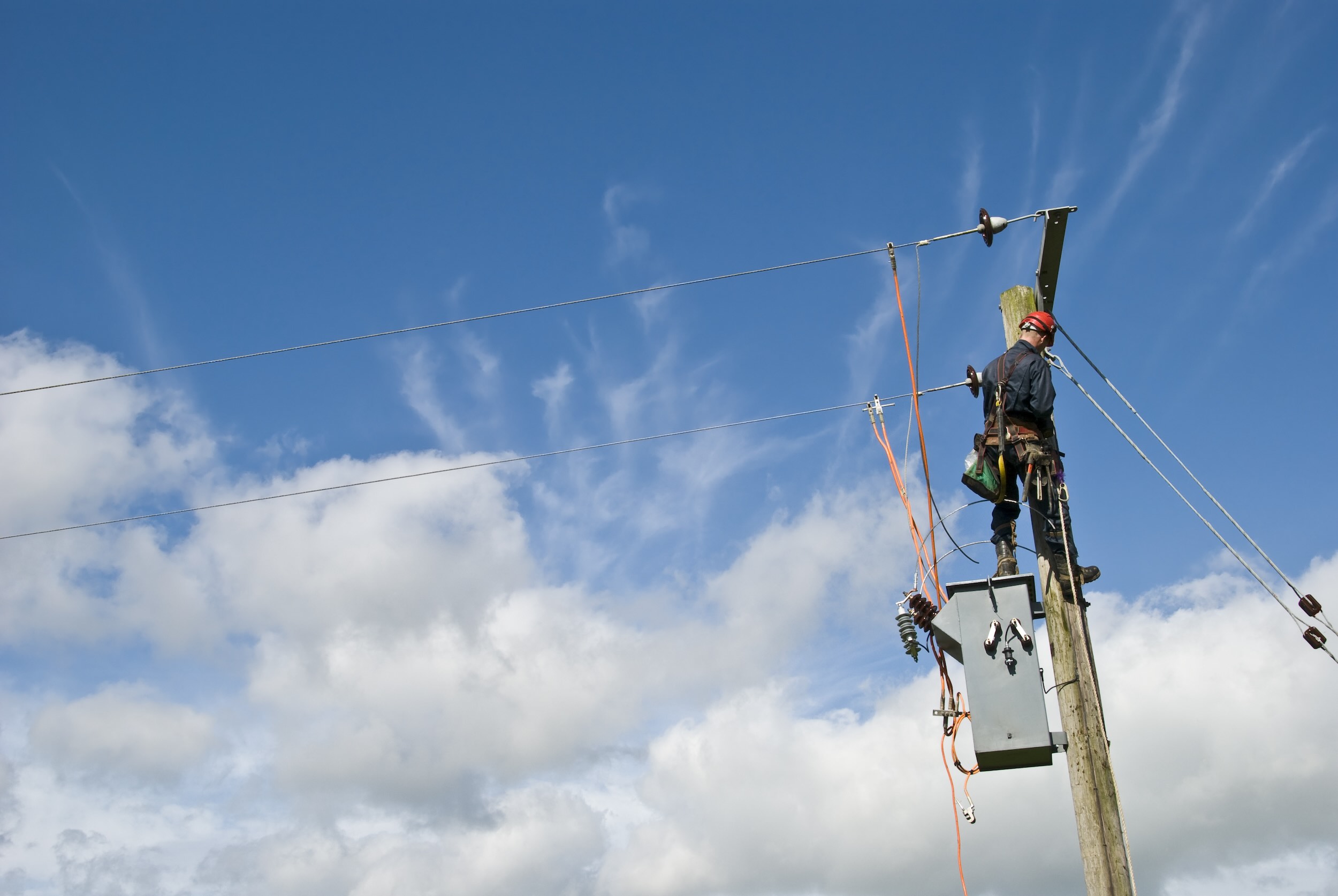 Travailleur des services publics réparant les lignes électriques sous un ciel bleu