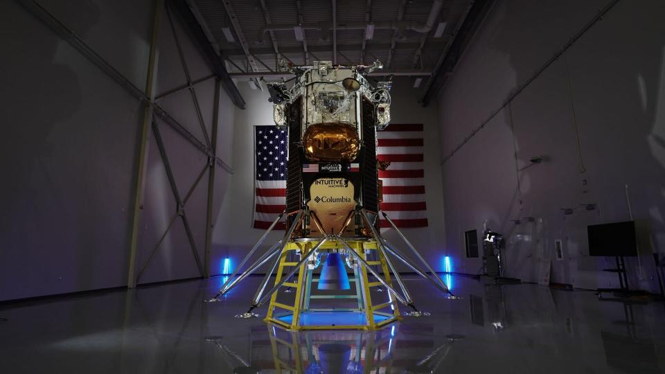 L'atterrisseur Odysseus Nova-C d'Intuitive Machines est photographié devant un drapeau américain dans un entrepôt faiblement éclairé.