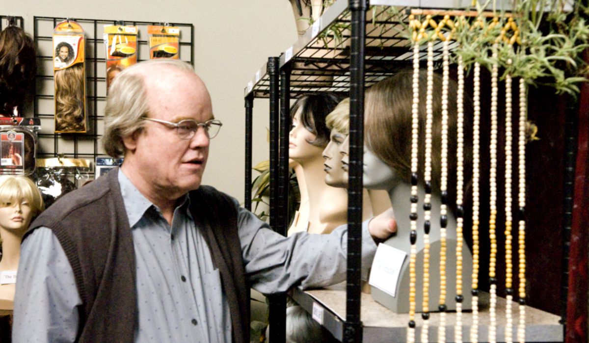 Le directeur de théâtre Caden (Philip Seymour Hoffman), un homme chauve et vieillissant portant des lunettes, regarde une exposition de têtes de mannequins avec des perruques dans les coulisses d'une pièce de théâtre à Synecdoche, New York.