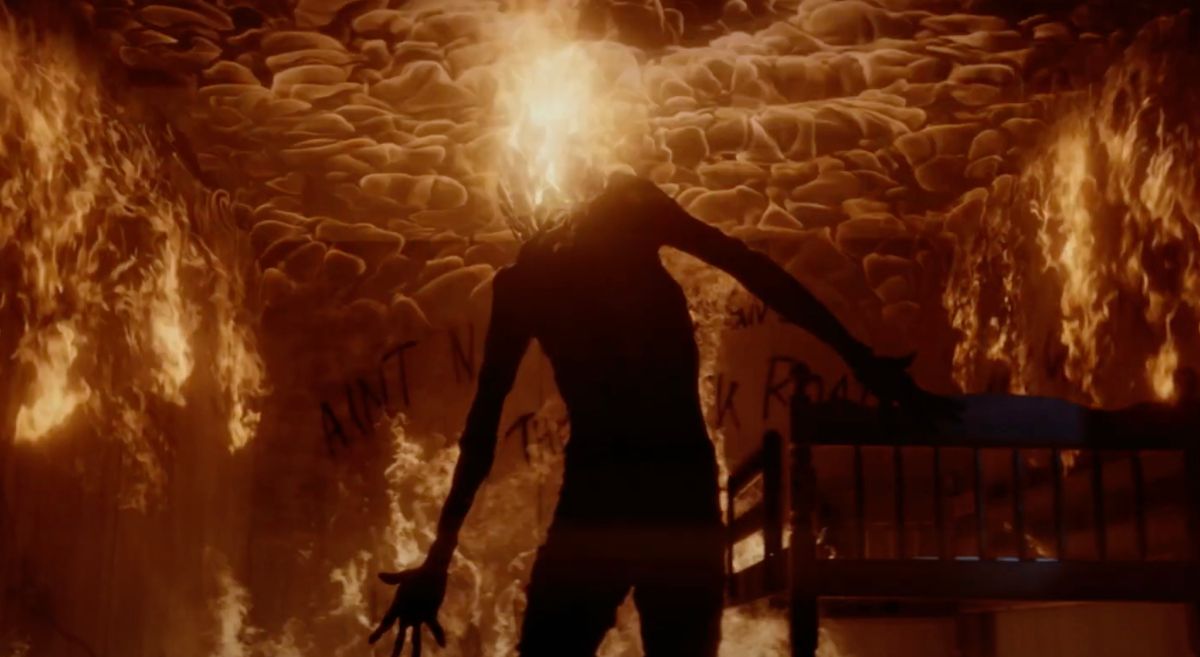 Une silhouette sans tête se tient dans une pièce en proie aux flammes, un panache de feu jaillissant de son cou dans Dark Harvest.