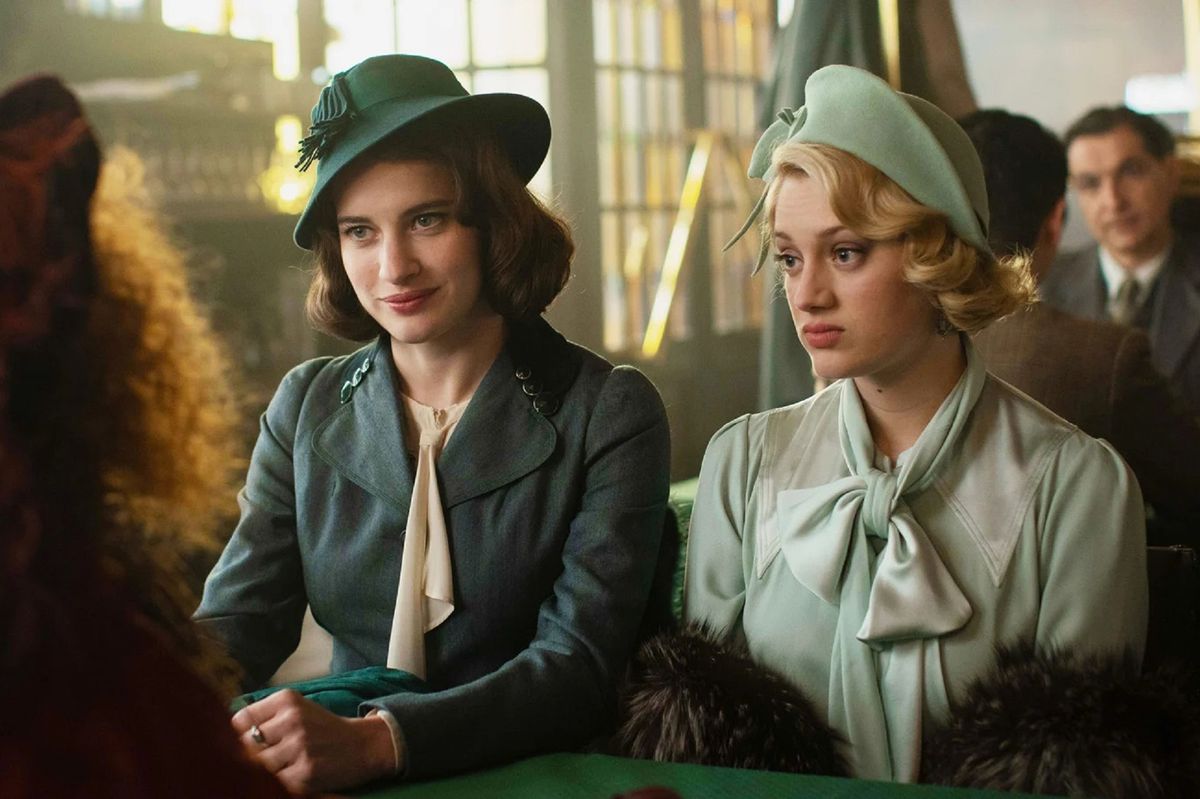 Deux femmes en manteaux et chapeaux verts assises l'une à côté de l'autre à une table.
