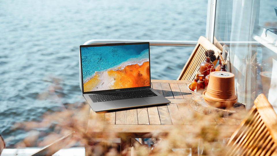 Image marketing de style de vie de l'Acer Swift Go 14 posé sur une table extérieure en bord de plage.