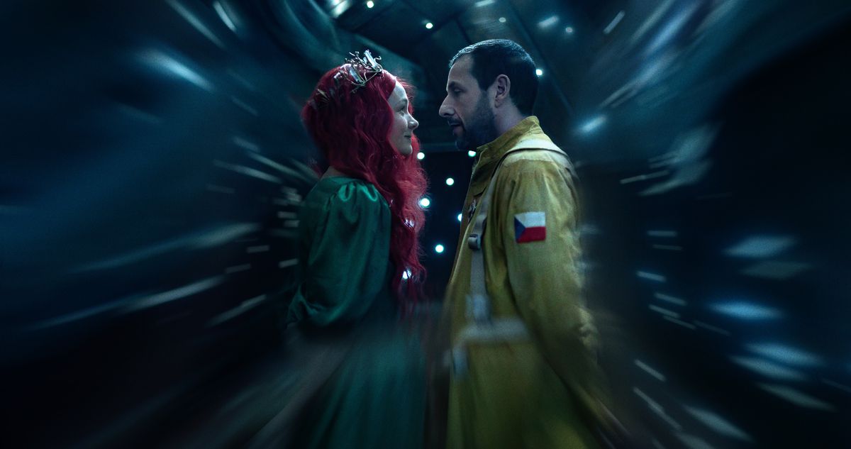 Lenka (Carey Mulligan, avec un diadème argenté, une perruque rouge fluide et une robe de bal verte) se tient près de Jakub (Adam Sandler), habillé en astronaute dans une combinaison de vol jaune, alors que tout autour d'eux se brouille dans une scène de Spaceman de Netflix.