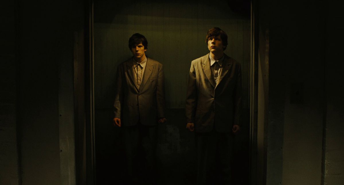 Deux Jesses Eisenberg se tiennent ensemble dans un ascenseur dans The Double