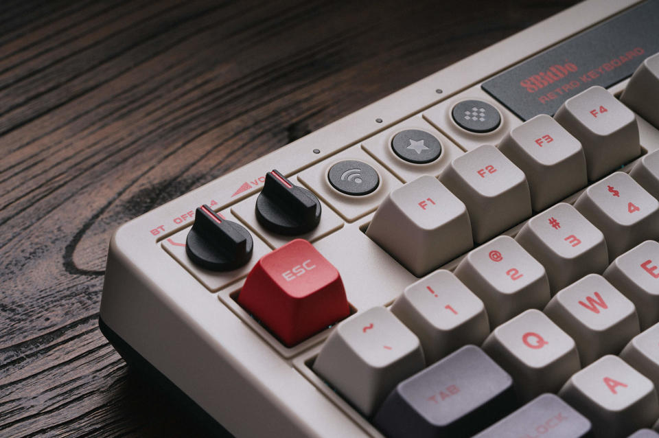 Photo du produit du clavier mécanique rétro 8BitDo.  Gros plan du coin supérieur gauche du clavier.  Il possède des interrupteurs noirs et des touches blanc cassé, rouges ou gris foncé.