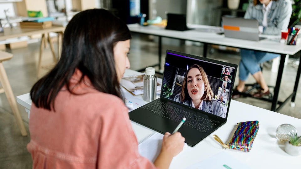 Une personne assise à une table, effectuant un appel vidéo avec une autre personne sur l'Acer Swift Edge 16. Espace de travail de bureau ouvert.