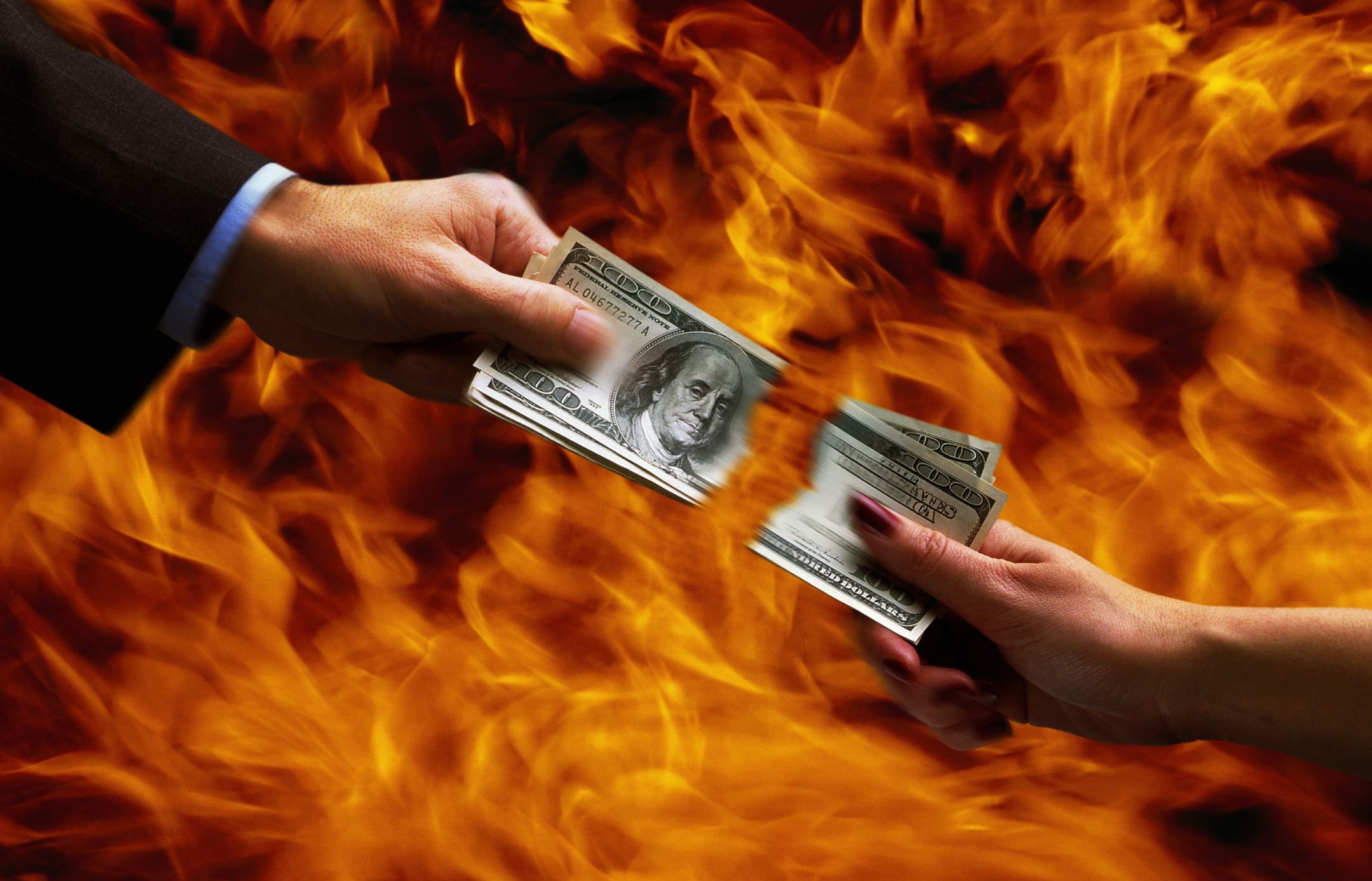 mains de deux personnes déchirant de l'argent avec des flammes en arrière-plan