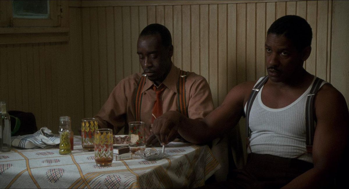 Denzel Washington et Don Cheadle sont assis l'un à côté de l'autre à une table pleine dans Le Diable en robe bleue