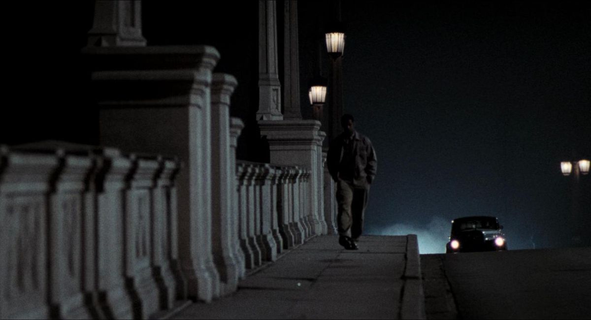 Denzel Washington marche le long d'un pont la nuit alors qu'une voiture approche dans Le Diable en robe bleue