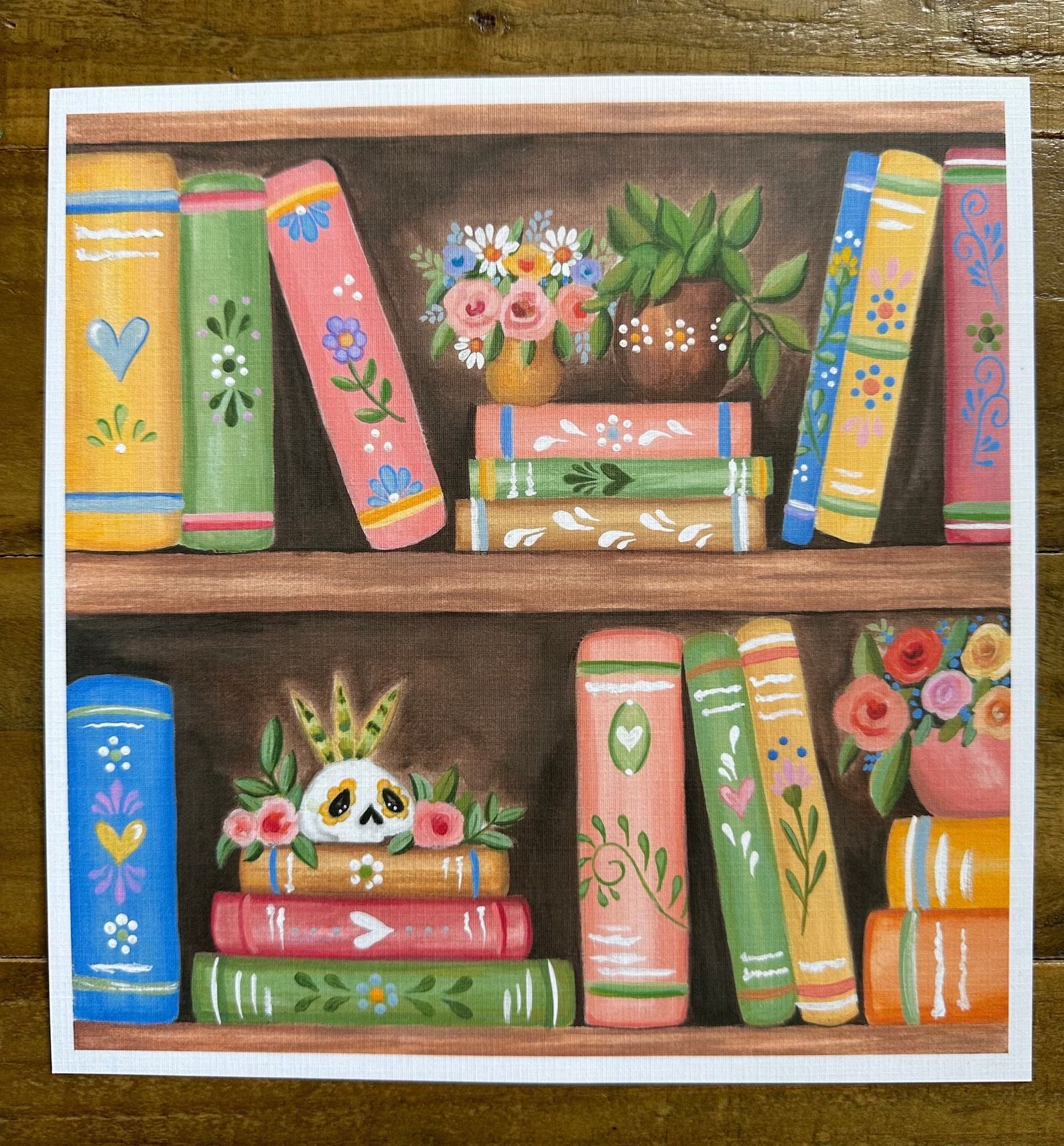 une impression montrant une étagère avec plusieurs livres colorés, des plantes succulentes et un crâne peint 
