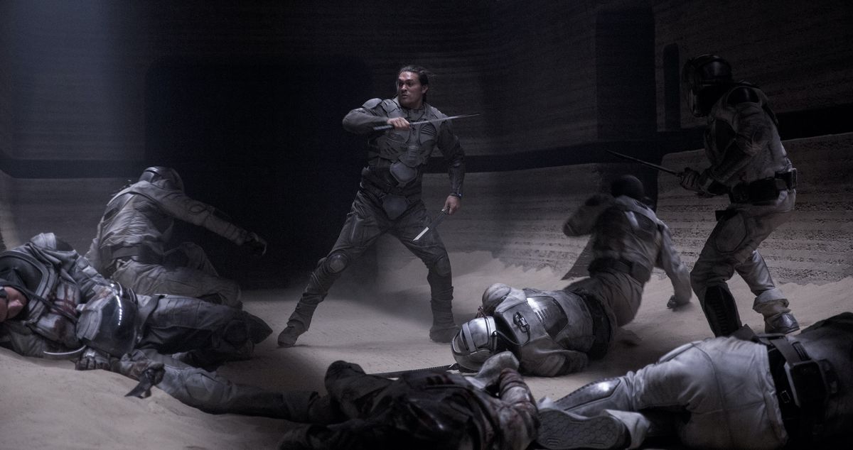 Jason Momoa dans le rôle de Duncan Idaho, brandissant deux lames et entouré de soldats effondrés ou effondrés en armure grise dans Dune