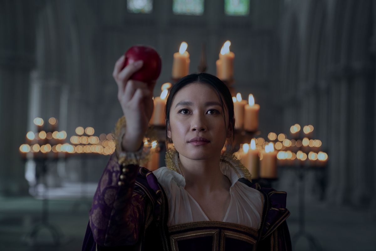 Jess Hong dans le rôle de Jin portant des vêtements de l'époque victorienne et tenant une pomme dans une salle du trône
