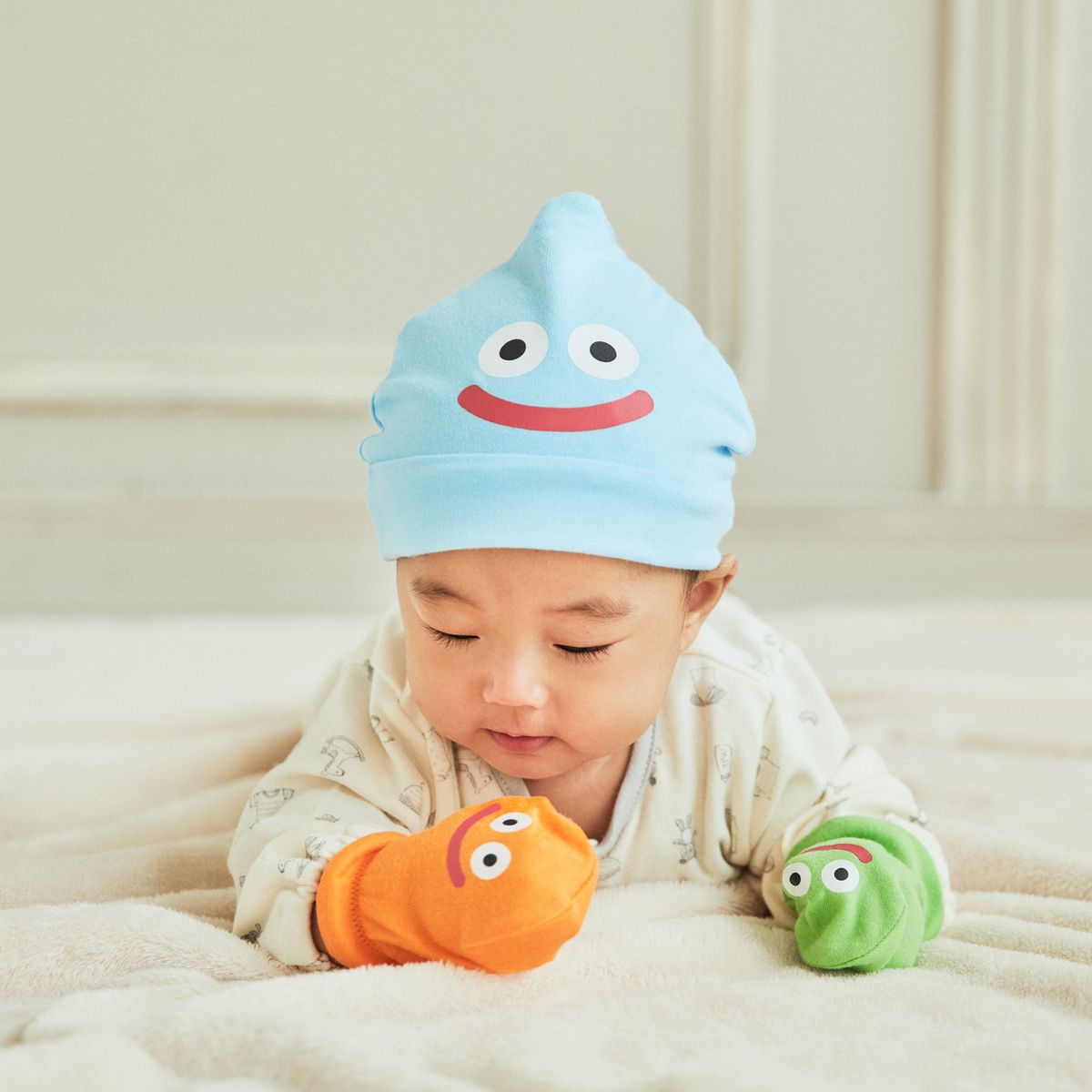 Un bébé portant des accessoires inspirés de Dragon Quest Slime, notamment un bonnet Slime et des mitaines Slime