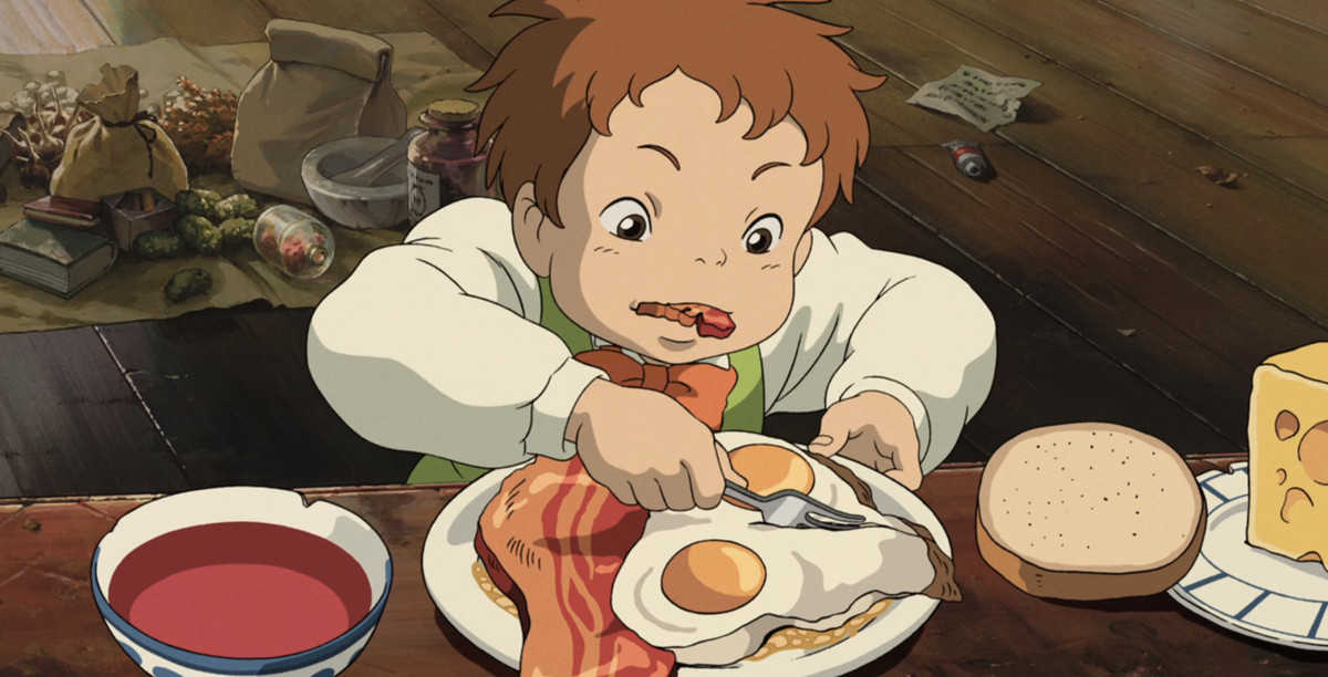 Un jeune garçon aux cheveux roux mâche un morceau de bacon épais tout en découpant ses œufs au plat avec une fourchette, dans une scène du Château ambulant du Studio Ghibli.