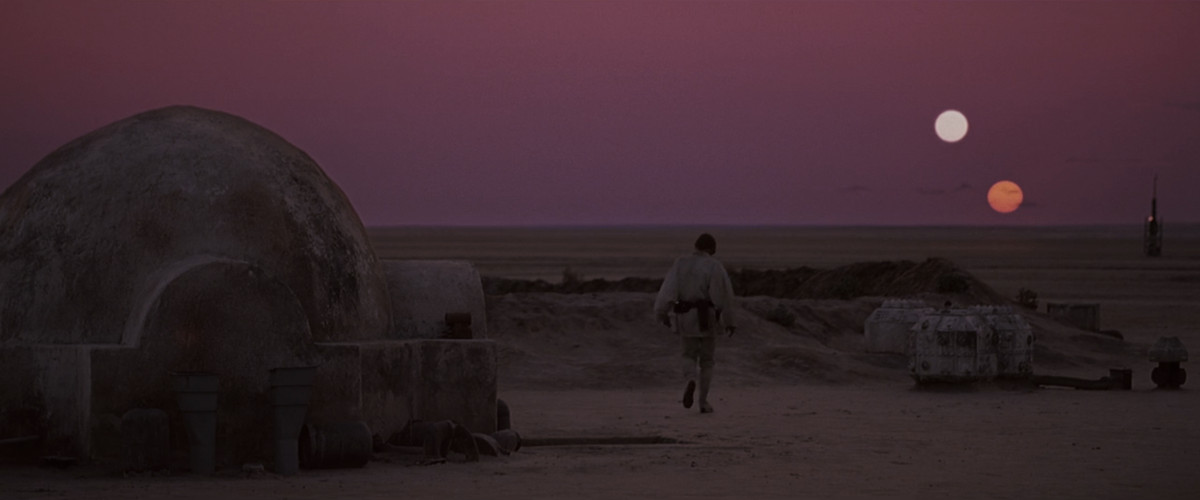 Luke Skywalker traverse sa cour sablonneuse en direction de l'horizon, deux soleils se couchant dans le ciel. 