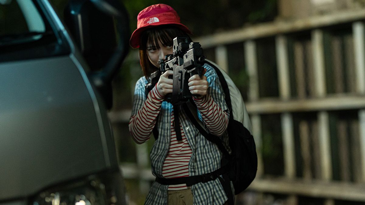 Une jeune fille portant un chapeau rouge et un sac à dos tient et vise une mitraillette dans Baby Assassins 2 Babies.